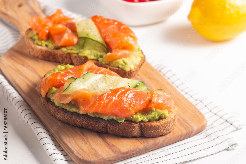 Two tasty open salmon sandwiches with avocado and cucumber. Morning healthy breakfast. Top view. Two tasty open salmon sandwiches with avocado and cucumber. Morning healthy breakfast. Top view.