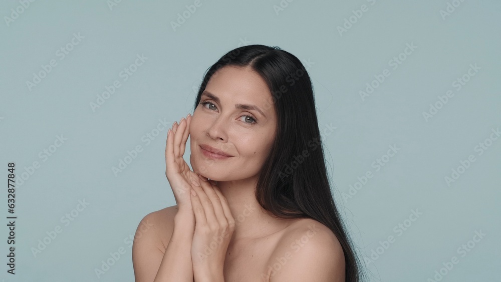 Obraz premium Portrait of a contented seminude woman on a blue background closeup. Woman with natural makeup, clean and smooth skin. Beauty concept. Natural beauty, cosmetology, skin care.