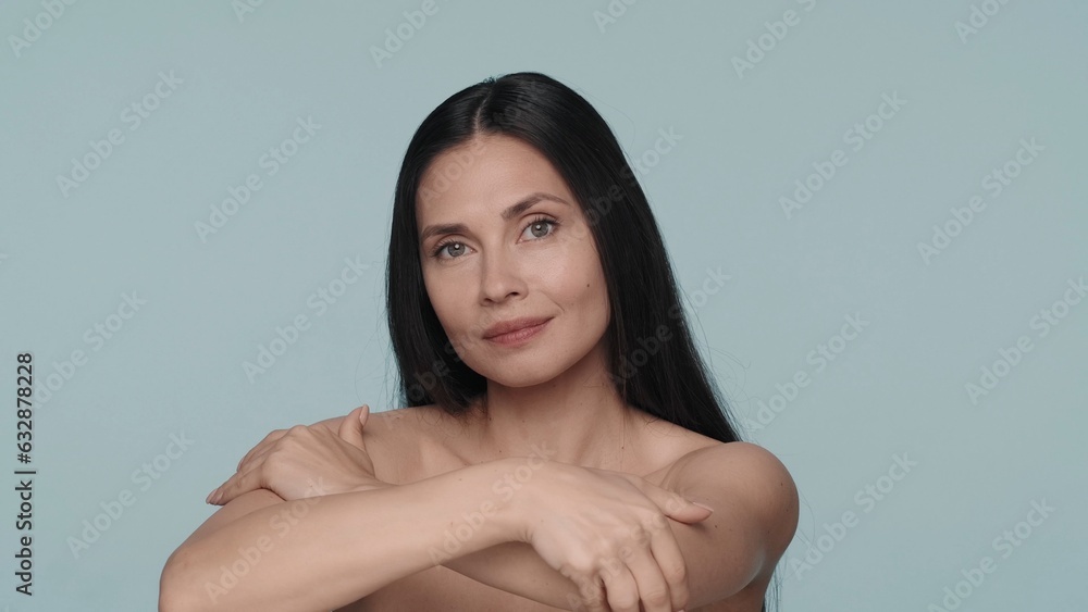 Portrait of a seminude smiling woman in the studio on a blue background close up. The woman hugs her shoulders, enjoying the perfection of her skin. Natural beauty, cosmetology, spa. Portrait of a seminude smiling woman in the studio on a blue background close up. The woman hugs her shoulders, enjoying the perfection of her skin. Natural beauty, cosmetology, spa.
