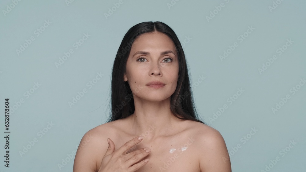 Obraz premium Body cream. The woman applies the cream to the chest area. Portrait of a seminude woman with clean, smooth skin on a blue background close up. The concept of beauty, cosmetology, skin and body care.