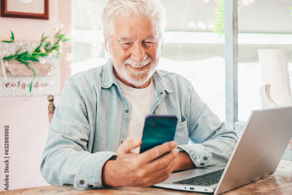 Smart work concept. Smiling senior man in coffee shop working on laptop while using mobile phone. Elderly man people enjoying free lifestyle doing job from remote Smart work concept. Smiling senior man in coffee shop working on laptop while using mobile phone. Elderly man people enjoying free lifestyle doing job from remote