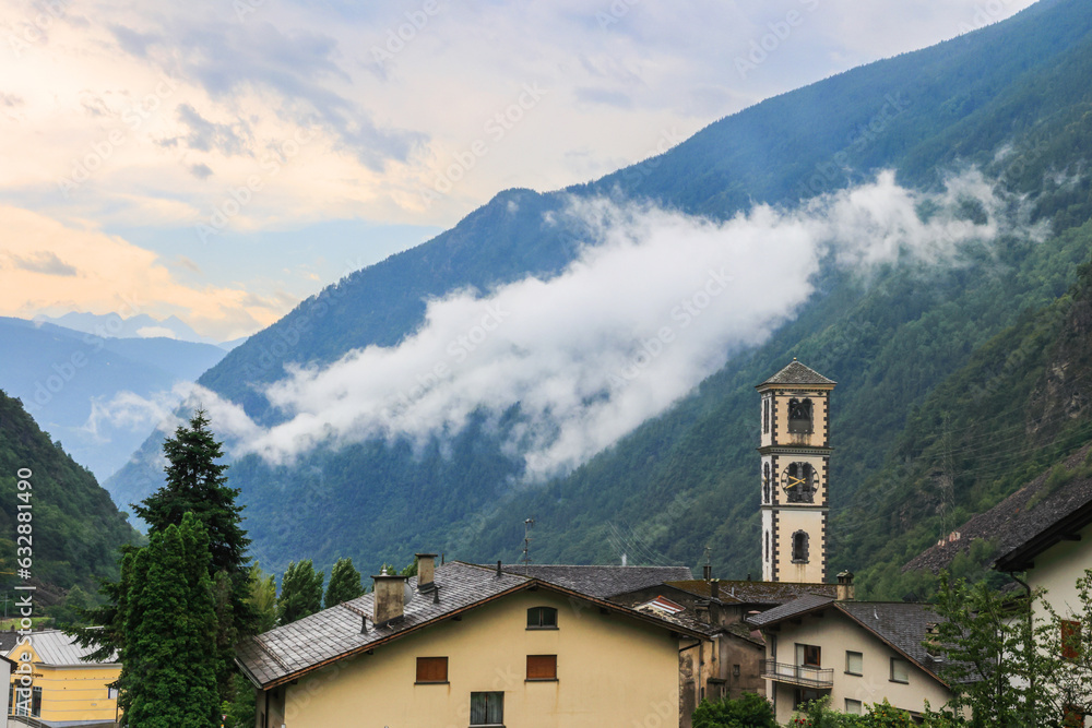 Tower of the Catholic church of San Carlo Borromeo in the Swiss town Brusio in the morning with fog stripe floating in the mountain background. The famous circle viaduct is built here.