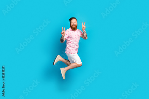 Full body photo of active carefree guy jumping hands fingers demonstrate v-sign empty space isolated on blue color background
