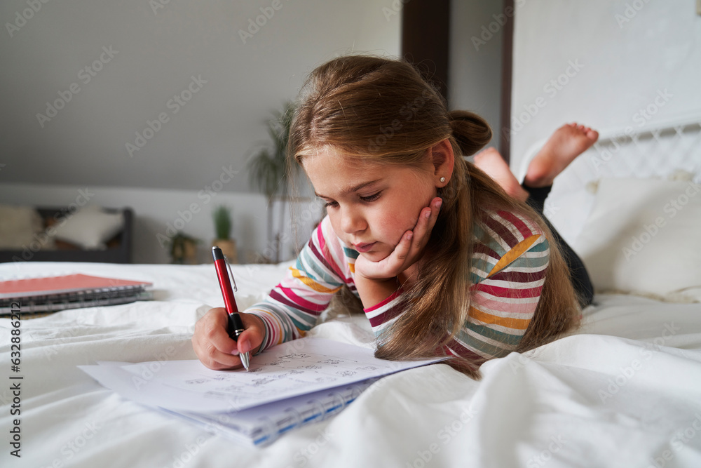 Elementary age girl studying while lying on front on the bed Elementary age girl studying while lying on front on the bed