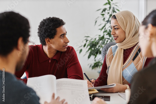 Group of modern Middle Eastern business people working together at meeting table in office and holding documents photo