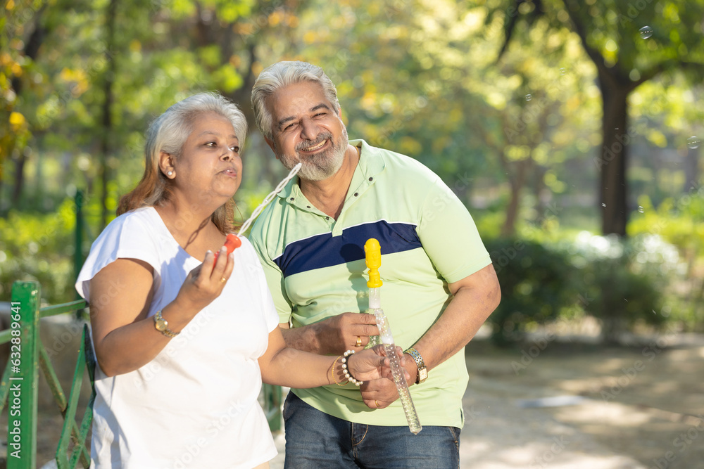 Happiness concept. indian senior couple blowing soap bubbles together in park.