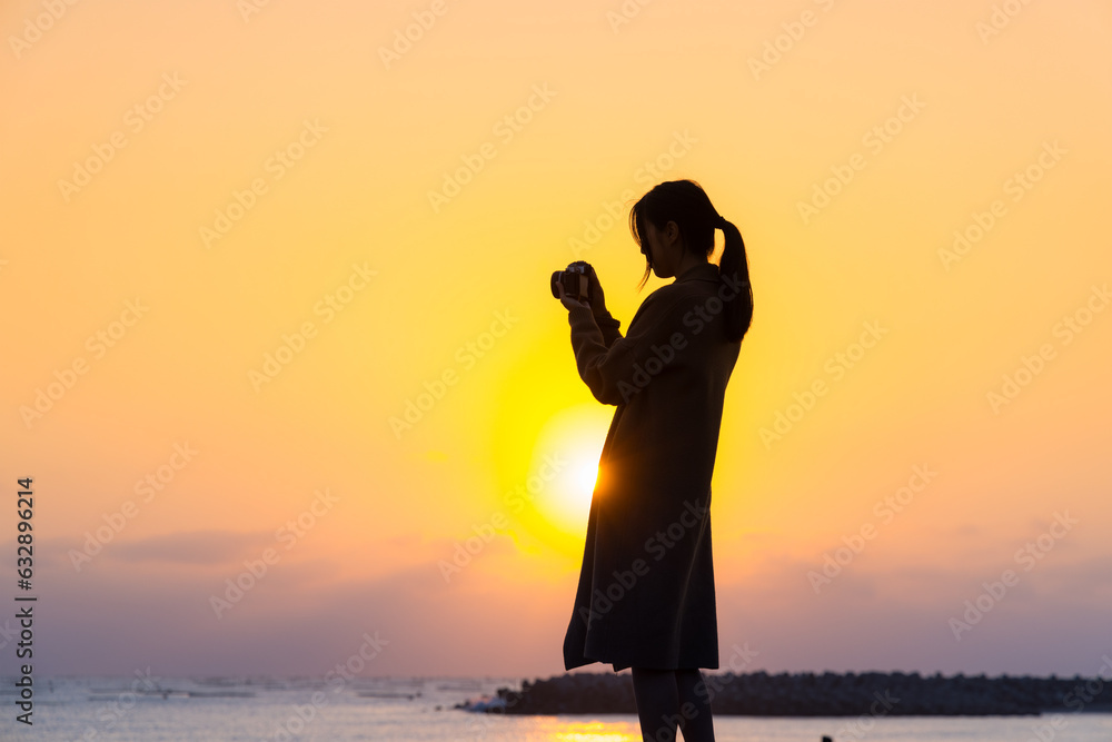 Silhouette of woman use camera to take photo at sunset in the beach
