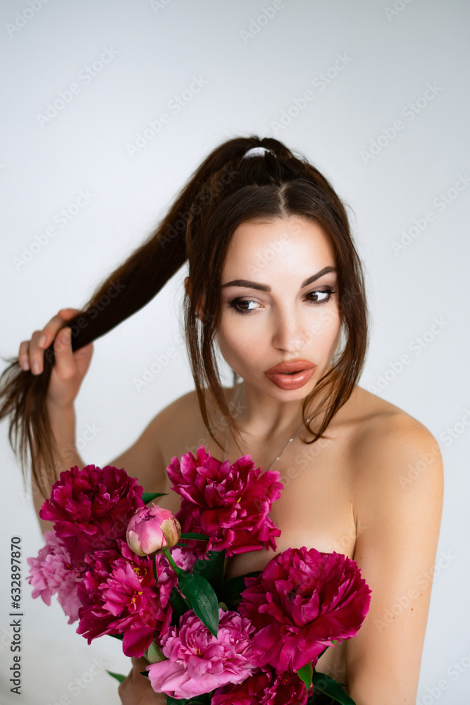 Young cheerful woman with beautiful bouquet of peonies lying on bed at home