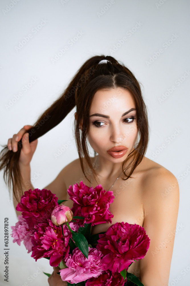 Young cheerful woman with beautiful bouquet of peonies lying on bed at home Young cheerful woman with beautiful bouquet of peonies lying on bed at home