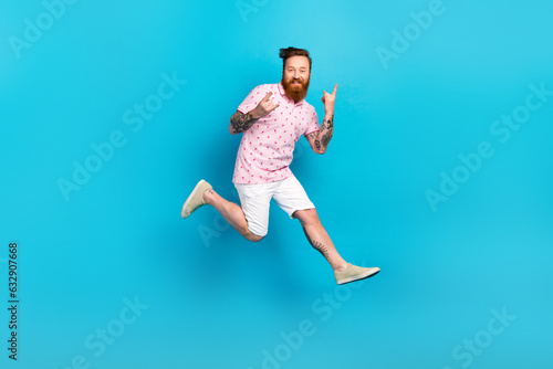 Full body profile photo of overjoyed eccentric man jumping fingers demonstrate heavy metal symbol isolated on blue color background