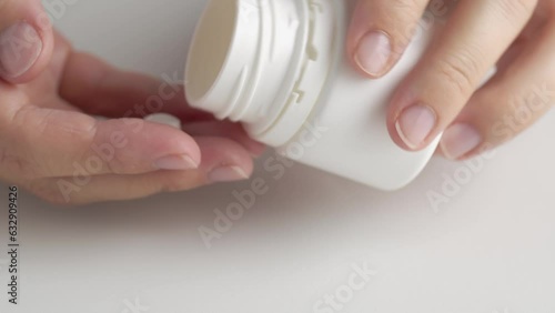 Hands opened a vial of pills. A woman pours pills or vitamins from a vial into the table.
