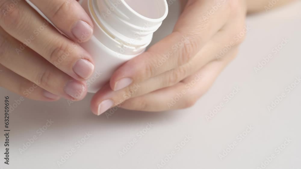 Hands open a vial of pink pills. Woman taking pills out of the bottle. A woman pours pills or vitamins from a jar into the palm of her hand. Hands open a vial of pink pills. Woman taking pills out of the bottle. A woman pours pills or vitamins from a jar into the palm of her hand.