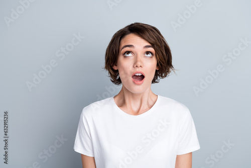 Photo of dreamy impressed woman dressed white t-shirt looking up empty space isolated grey color background
