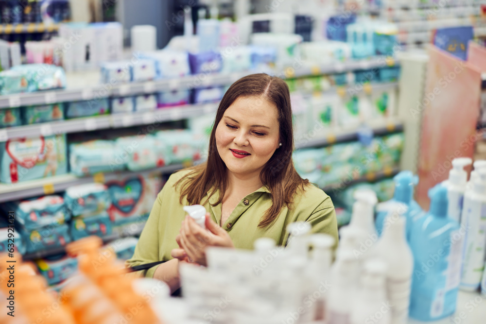 A smiling plus-size woman is shopping for a baby cream in a baby section.