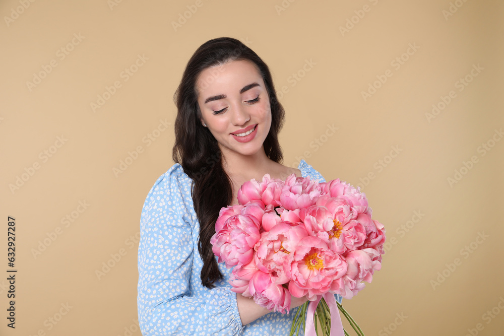 Beautiful young woman with bouquet of pink peonies on beige background