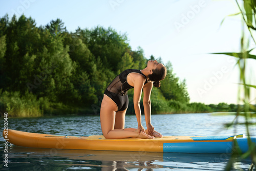 Young woman practicing yoga on color SUP board on river © New Africa