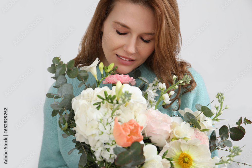 Beautiful woman with bouquet of flowers near white wall indoors, closeup