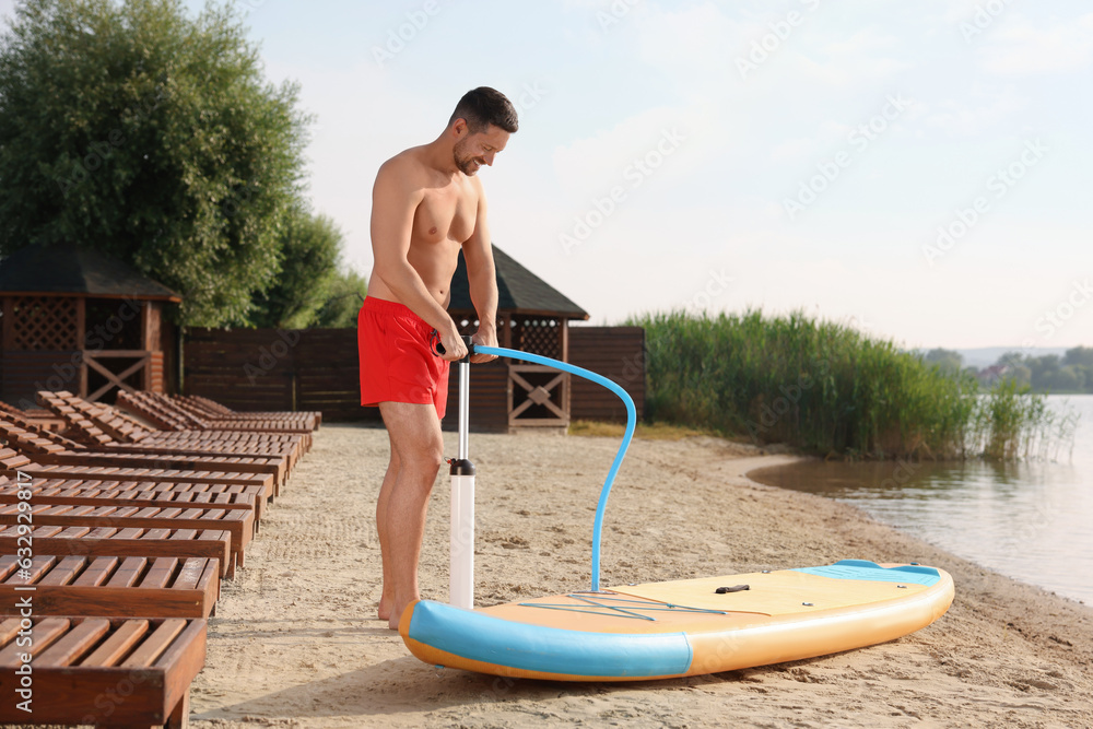 Fototapeta premium Man pumping up SUP board on river shore