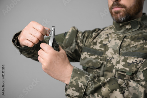 Soldier pulling safety pin out of hand grenade on light grey background, closeup. Military service