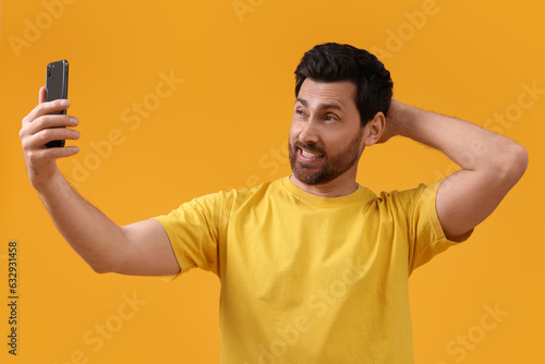 Emotional man taking selfie with smartphone on yellow background