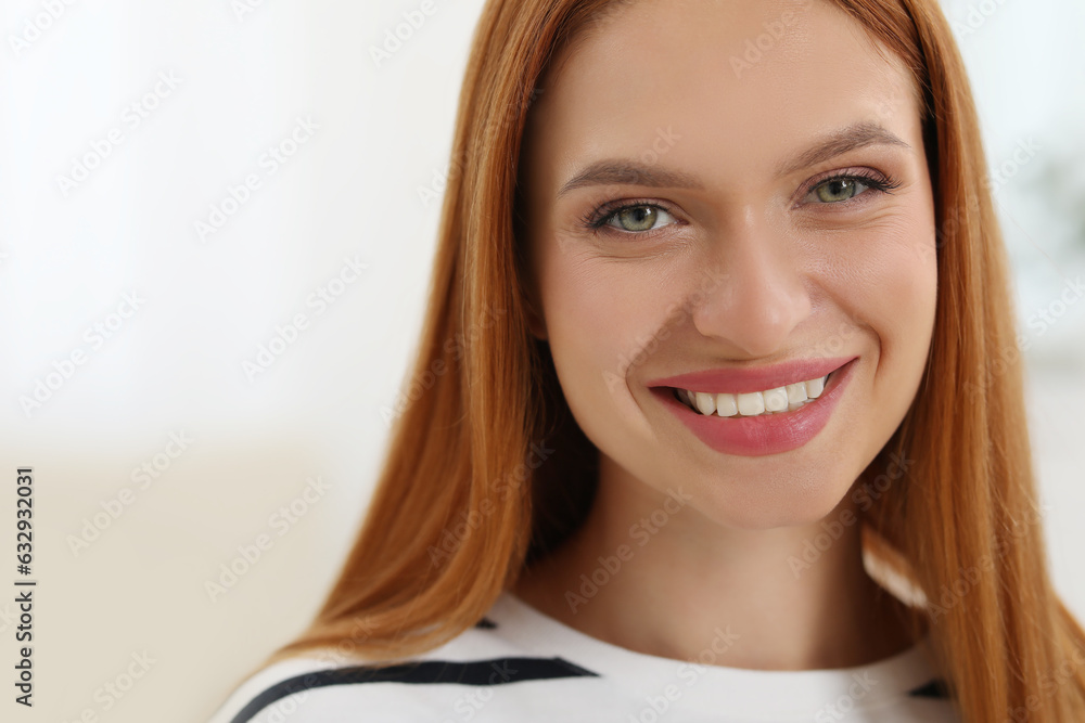 Portrait of beautiful young woman with red hair indoors. Attractive lady smiling and looking into camera. Space for text Portrait of beautiful young woman with red hair indoors. Attractive lady smiling and looking into camera. Space for text