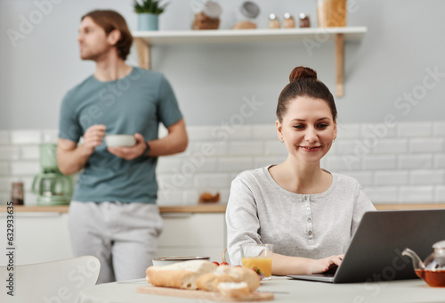 Portrait of smiling young woman using laptop in kitchen during breakfast, copy space