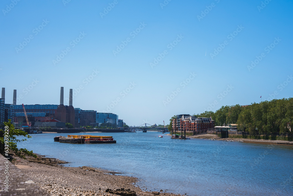 Battersea Power station at banks of Thames river. Boats moored on water with blue sky in background. Scenic view of nature in city during sunny day.
