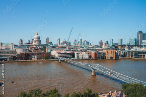 Millennium bridge over river Thames. Financial district with clear sky in background. Buildings in city during sunny day at London. photo