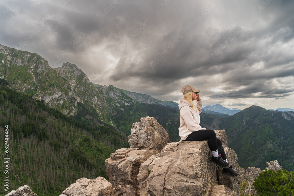 A girl sits on a rock in the Tatras on a summer evening, the sky is covered with clouds.