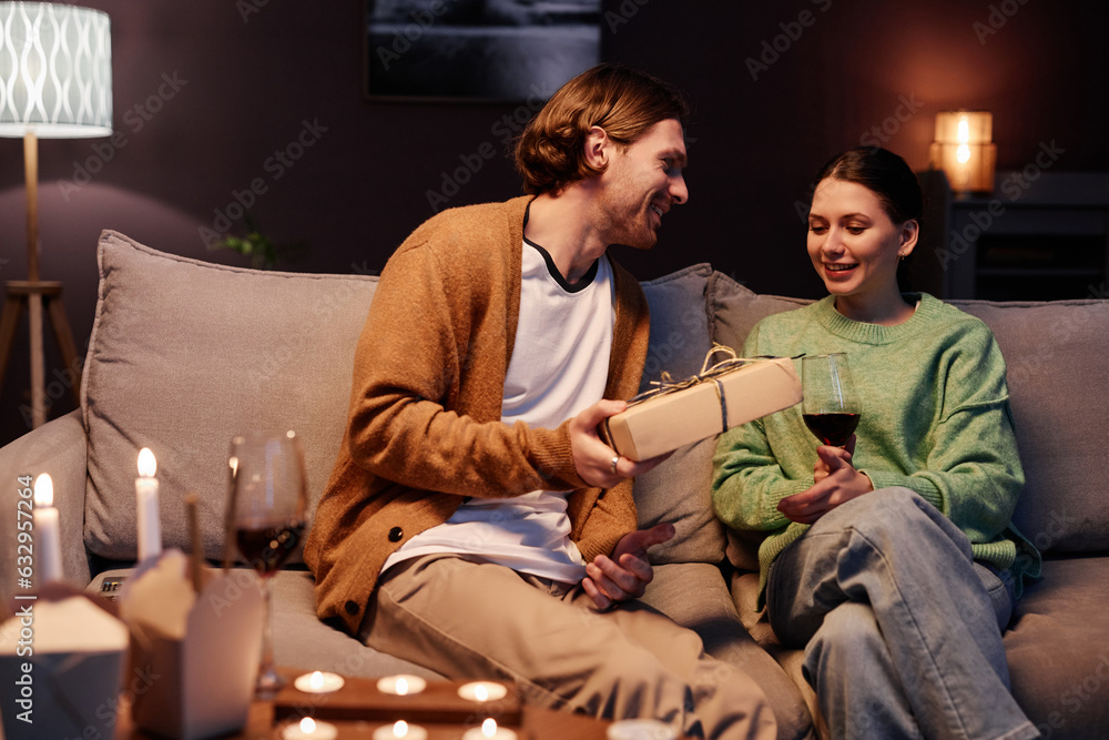 Portrait of young man giving present to wife or girlfriend while enjoying romantic evening at home