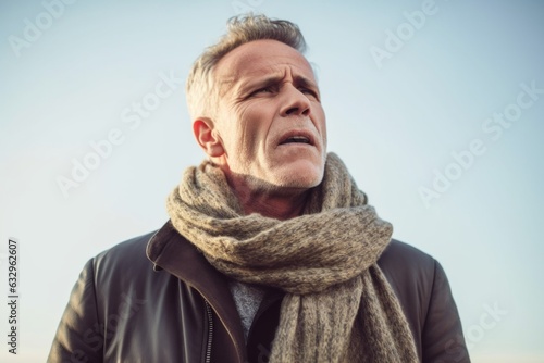 Group portrait photography of a man in his 50s grimacing and touching his throat due to strep throat wearing a charming scarf against a sky background  photo