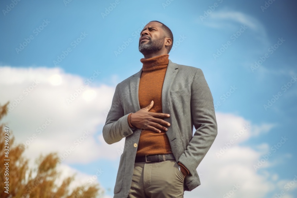 Medium shot portrait photography of a man in his 40s holding his stomach with discomfort from gastritis wearing a chic cardigan against a sky and clouds background 