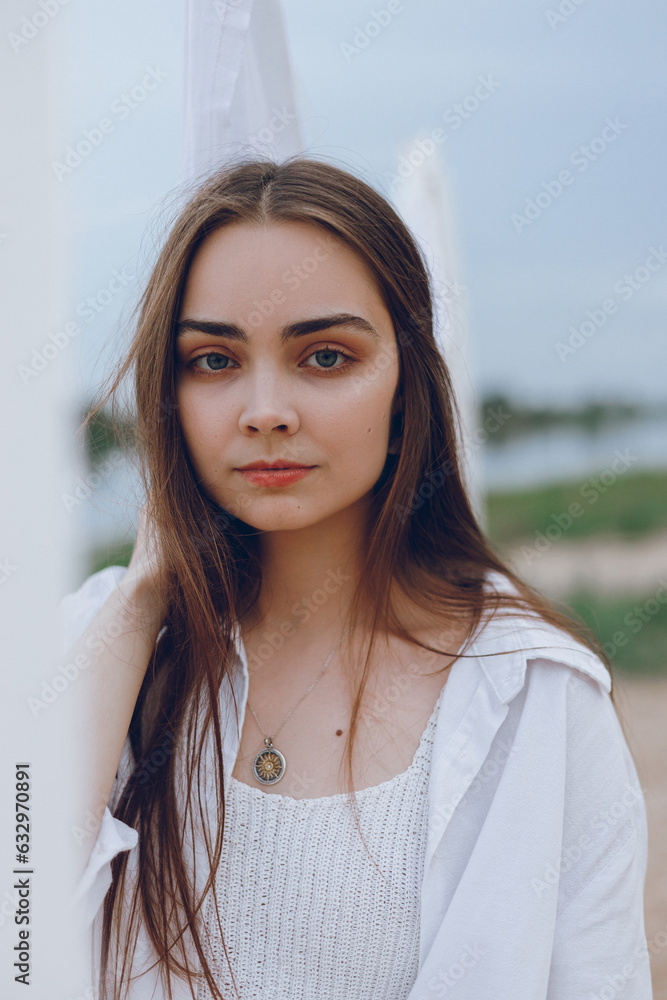 Portrait of beautiful woman with brown hair in white linen standing near dry laundry outdoors and looking at camera Portrait of beautiful woman with brown hair in white linen standing near dry laundry outdoors and looking at camera
