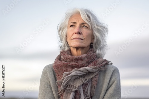 Lifestyle portrait photography of a woman in her 60s showing tiredness and a worn-down expression due to chronic fatigue syndrome wearing a cozy sweater against a sky and clouds background  photo