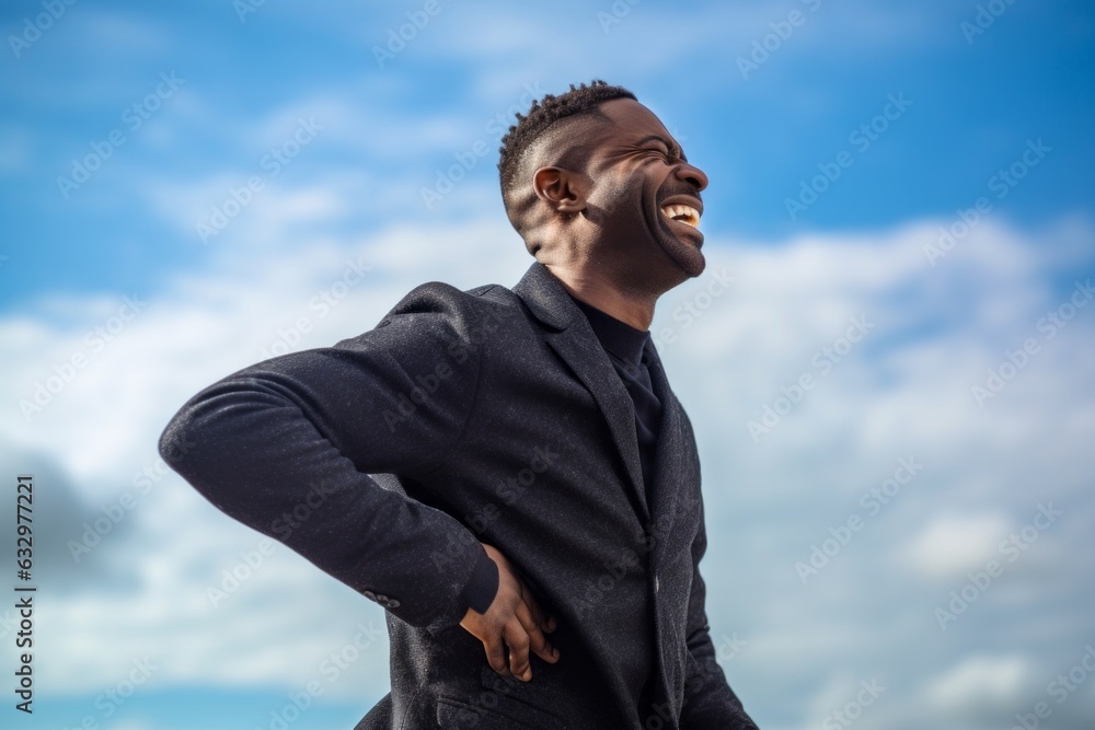 Medium shot portrait photography of a man in his 30s wincing with pain and holding his lower back due to sciatica wearing a chic cardigan against a sky and clouds background Medium shot portrait photography of a man in his 30s wincing with pain and holding his lower back due to sciatica wearing a chic cardigan against a sky and clouds background