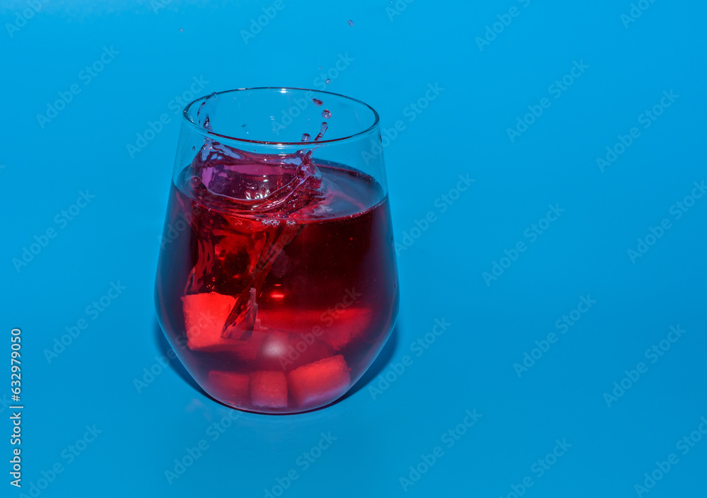 Izolowana szklanka z czerwonym zimnym napojem, wrzucać kostki lodu - obrazy, fototapety, plakaty 