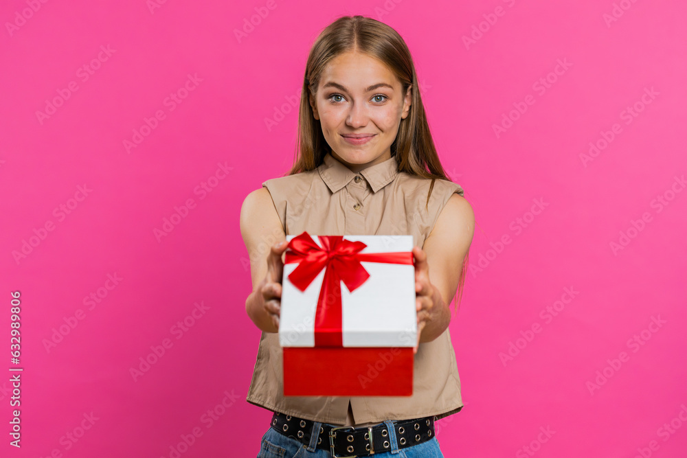Fototapeta premium Positive smiling young woman presenting birthday green gift box stretches out hands, offer wrapped present career bonus, celebrating party, sale. Blonde girl isolated alone on pink studio background