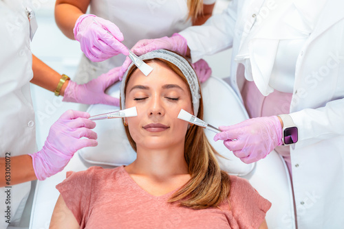 Three doctors and cosmeticians doing multiple facial treatments on a young  woman's face