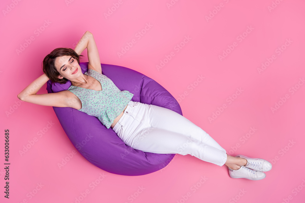 Full body photo of young careless student lady take nap hands head lying bean bag comfortable relax place isolated on pink color background Full body photo of young careless student lady take nap hands head lying bean bag comfortable relax place isolated on pink color background