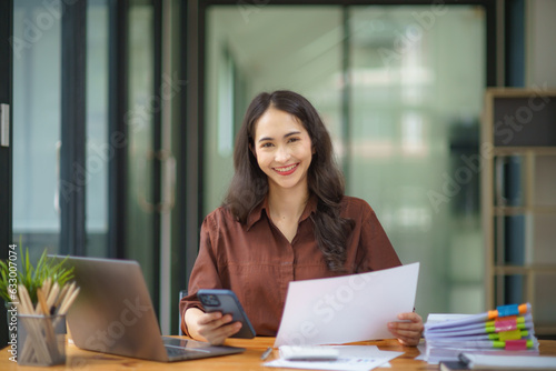 Happy beautiful smiling Asian businesswoman holding a mobile phone while working in an office.