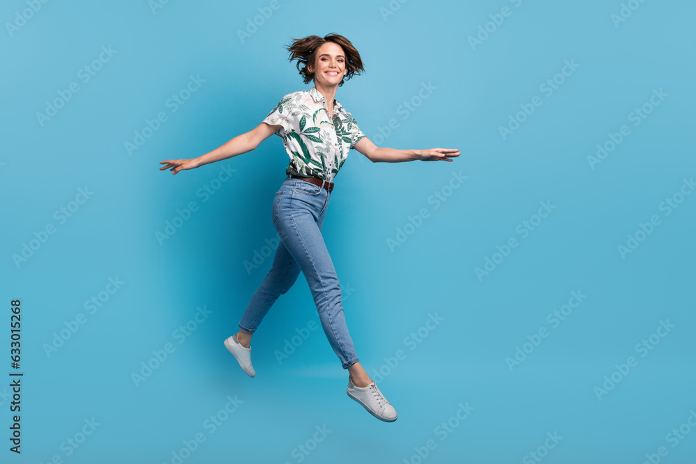Full length photo of positive pretty woman dressed print shirt jumping high walking empty space isolated blue color background