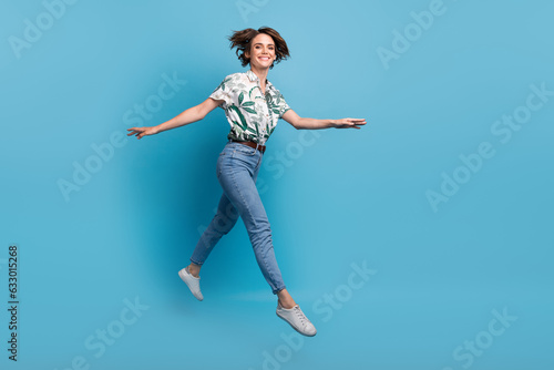 Fototapeta Naklejka Na Ścianę i Meble -  Full length photo of positive pretty woman dressed print shirt jumping high walking empty space isolated blue color background