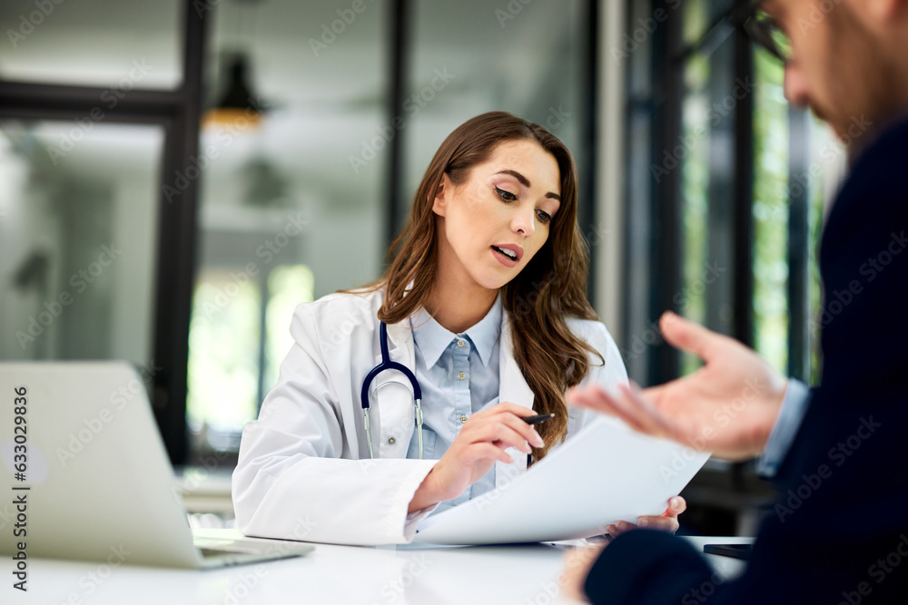 A brunette female doctor reading male patients' results and sitting at the table. A brunette female doctor reading male patients' results and sitting at the table.