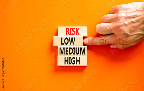 Time to low risk symbol. Concept word Risk low medium high on wooden block. Businessman hand. Beautiful orange table orange background. Business time to low risk concept. Copy space.