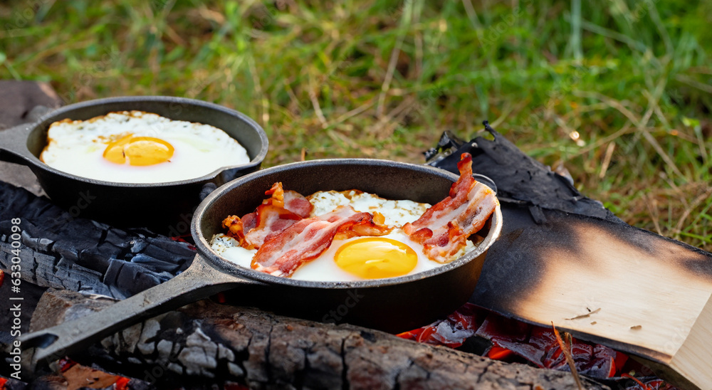 delicious eggs with bacon cooking on firewood outdoors in a black cauldron