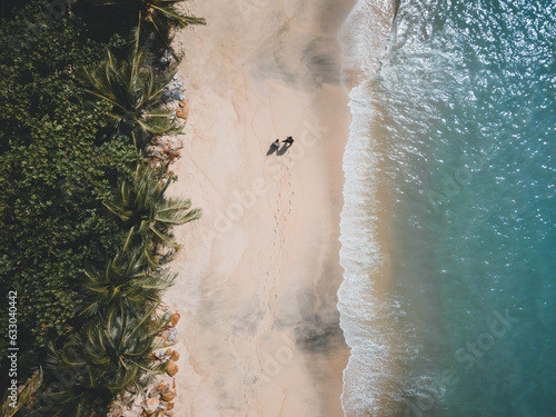 Married couple holding hands walking along the beach with wedding suit and gown.	
