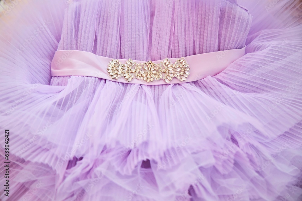 A lilac-colored baby dress and an embroidered belt. Close-up of clothes. A lilac-colored baby dress and an embroidered belt. Close-up of clothes.