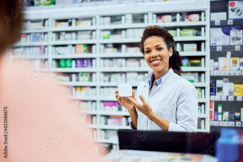 A female African pharmacist holding a pharmacy product and showing it to a customer.