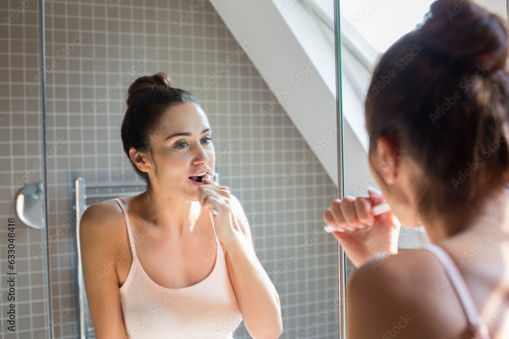 Mid adult woman brushing teeth in bathroom mirror. Mid adult woman brushing teeth in bathroom mirror.