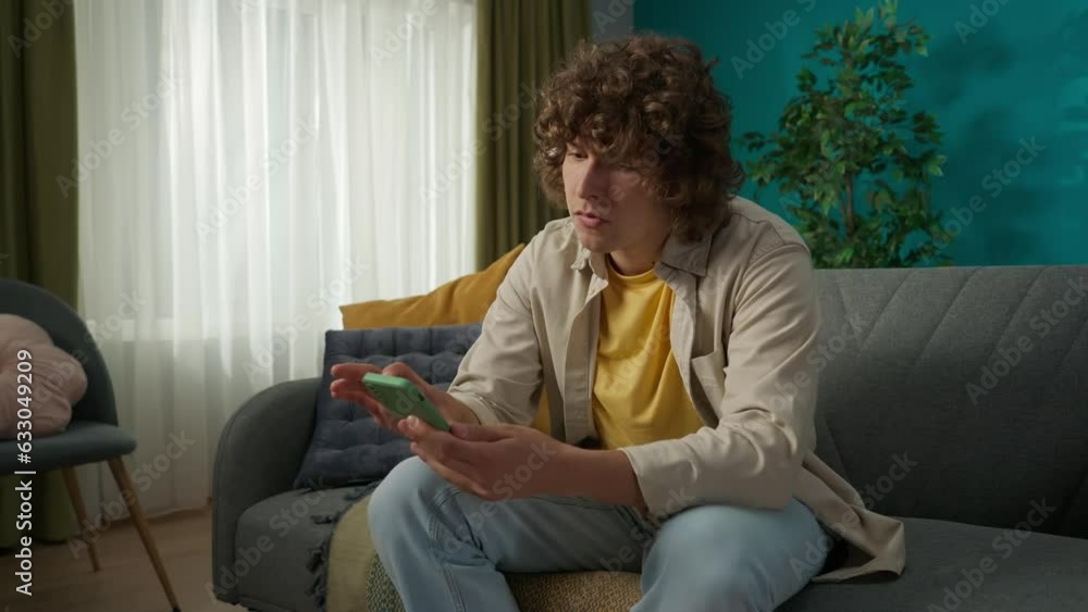 Young man sitting on the sofa in the living room and scrolling through his smartphone, closeup shot Young man sitting on the sofa in the living room and scrolling through his smartphone, closeup shot